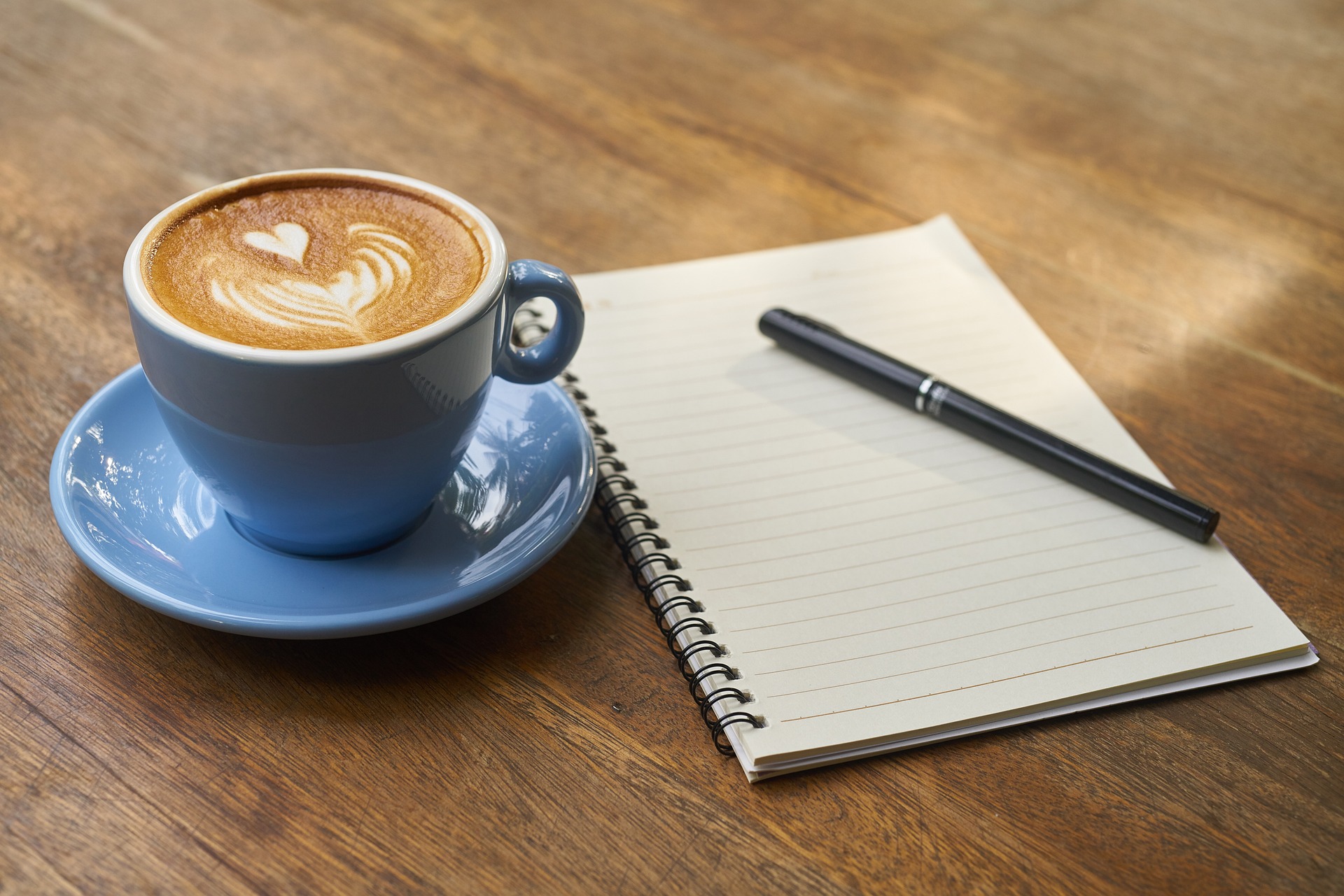 A cup of coffee beside a notebook on top of a wooden desk